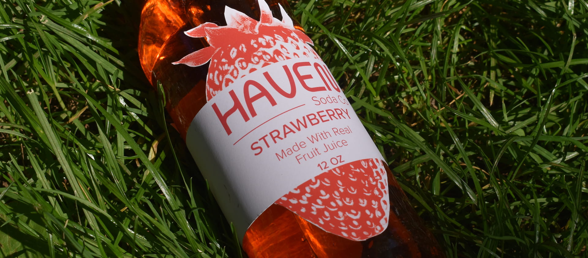 Haven strawberry soda bottle laying in grass.